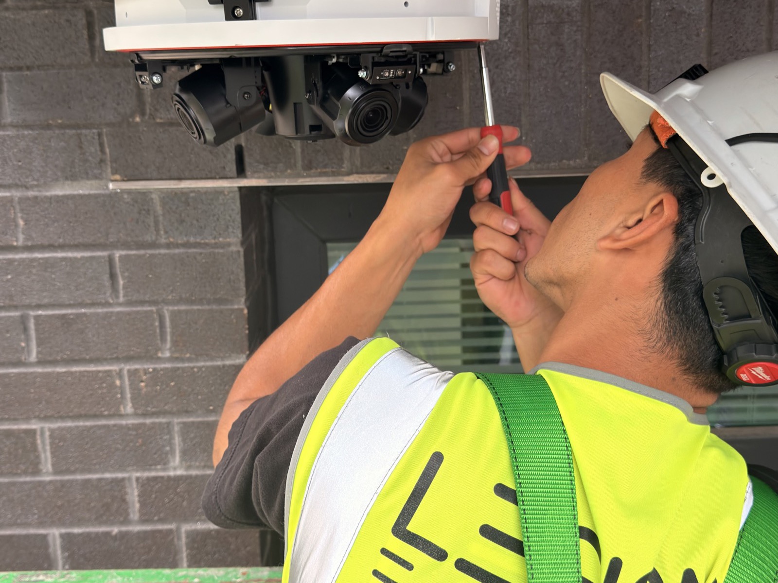 Legion E-Solutions technician in a branded hi-vis vest and hard hat adjusting a multi-sensor camera mounted under a soffit